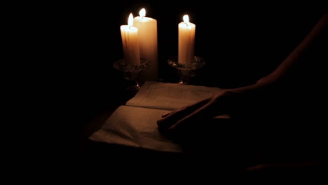Turning-the-Pages-of-Holy-Book-Lit-by-Candle-Light-in-a-Hidden,-Dark-Place