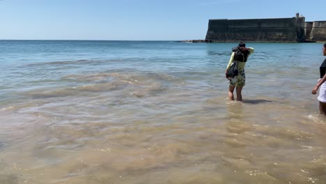 Charmante-Frau-Taucht-Ihre-Füße-Am-Strand-Von-Oeiras-Ins-Wasser-Und-Trägt-Ein-Sehr-Stilvolles-Kleid-An-Einem-Sonnigen-Tag,-Portugal-Tourismus