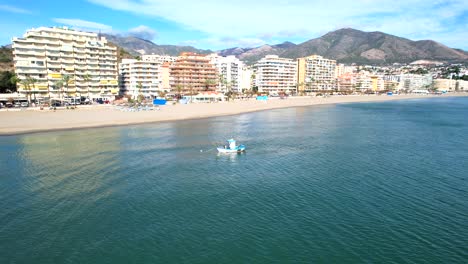Aerial-pan-across-fuengirola-hills-beach-with-small-tug-boat