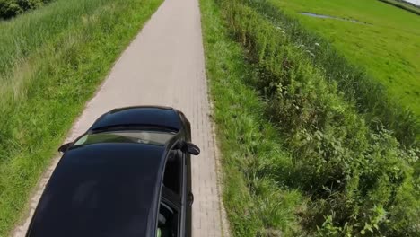 black-car-drives-along-a-small-path-between-fields