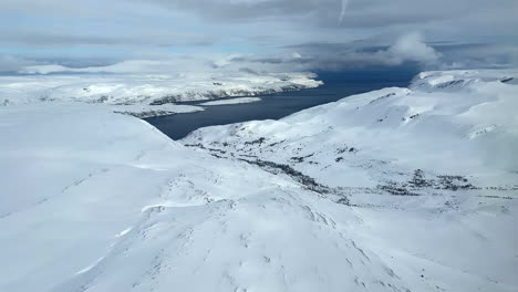 Aerial-view-of-snow-covered-mountains,-clouds-and-a-Norwegian-fjord-In-Northern-Norway,-Finnmark