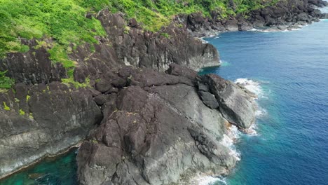 Aerial-Orbit-of-Sharp-Jagged-Basalt-Rocks-along-Tropical-Island-with-lush-greenery-and-turquoise-ocean-waters