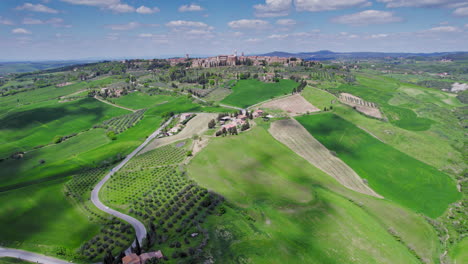 Town-of-Pienza-by-olive-plantations-in-Tuscany,-wide-forward-aerial