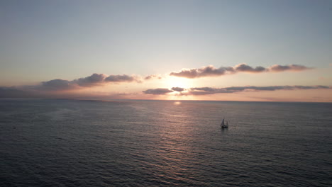 Tranquil-Dawn-with-Sailboat-and-Rising-Sun:-A-Serene-Ocean-Voyage---Aerial-Drone-Video