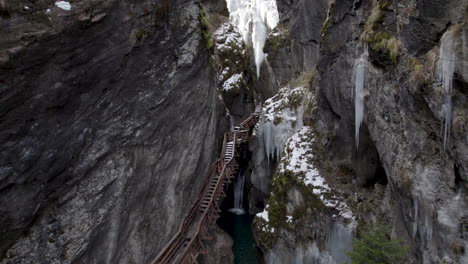 Drone-flying-backwards-between-two-cliffs-with-a-small-river-with-icicles-on-the-walls-and-a-staircase-going-up-in-Austria-at-the-Sigmund-Thun-Klamm