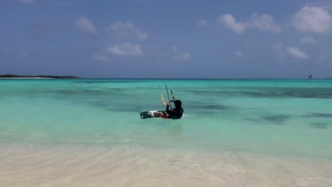 Man-lying-on-shallow-water-put-kite-board-and-start-to-fly-kitesurf,-slow-motion