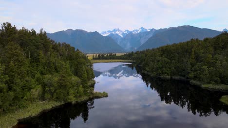 High-snowy-mountain-peaks-of-New-Zealand-reflected-in-still-water-of-Lake-Matheson,-Fox-Glacier