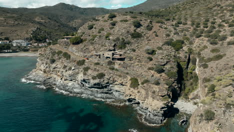 Remote-villa-on-lake-coastline-and-rocky-cliffs,-aerial-drone-view