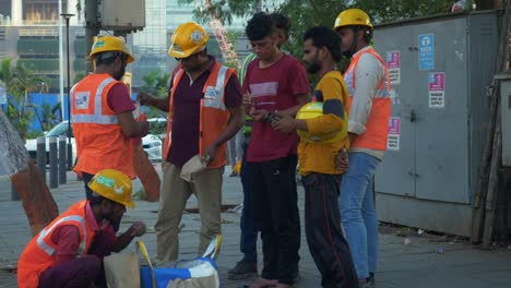 Group-of-Indian-male-construction-and-factory-workers-in-safety-uniform-taking-evening-snack-break,-Bandra-Kurla-Complex,-Mumbai