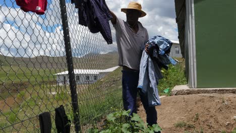 African-man-pulls-clean-and-dry-laundry-from-chain-link-fence,-Lesotho