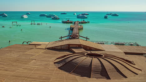 High-angle-shot-over-tourists-walking-around-on-wooden-pier-surrounded-by-beautiful-turquoise-sea-water-on-a-sunny-day-in-timelapse