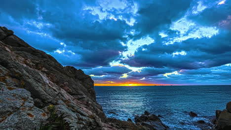 Timelapse-of-golden-sunset-sky-with-moving-clouds-over-ocean-and-sea-rocks