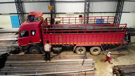Factory-worker-loading-truck-with-heavy-steel-beams,-India