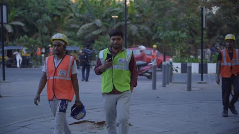 Dos-Trabajadores-Indios-Del-Sitio-De-Construcción-Con-Uniforme-De-Seguridad-Caminando-Por-La-Carretera-Después-De-Que-Termina-El-Turno-De-Trabajo,-Complejo-Bandra-Kurla,-Mumbai