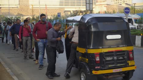 Indian-corporate-people-standing-in-queue-to-take-autorickshaws-for-commuting-after-office-hour-ends-with-Jio-World-Centre-building-in-background,-Mumbai