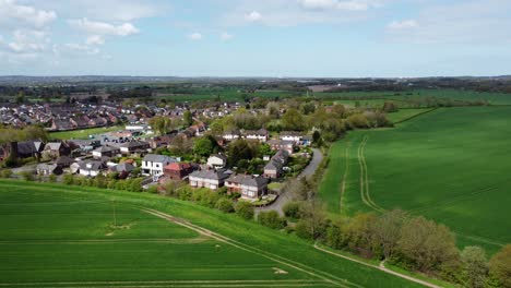 Establishing-aerial-view-rural-British-countryside-village-surrounded-by-farmland-fields,-Cheshire,-England