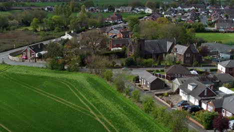 Aerial-view-rural-British-countryside-village-church-surrounded-by-farmland-fields,-Cheshire,-England