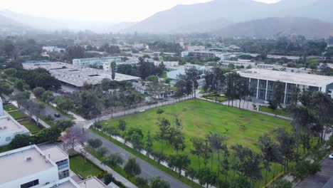 Drone-flies-over-the-National-Agrarian-University-or-in-Spanish,-"Universidad-Nacional-Agraria-La-Molina"-Many-green-trees-and-mountains-in-the-background