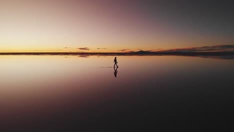 Aerial-of-a-lone-figure-walking-along-the-mirrored-reflection-of-the-world's-largest-salt-flat-at-dusk-in-Uyuni-Salt-Flats-,-Bolivia