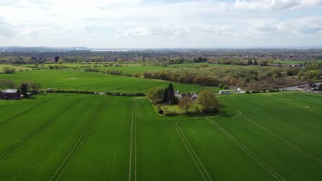Rural-British-farmhouse-aerial-view-surrounded-by-lush-green-trees-and-agricultural-farmland-countryside-crop-fields