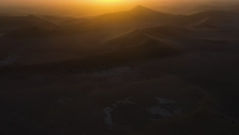 Aerial-tilt-reveal-of-a-hazy-sunset-above-desert-sand-dunes-in-Africa