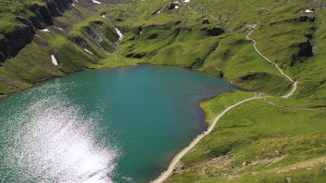 Aerial-flying-over-:-Summer-Sun-glitter-on-water-surface-of-Bachalpsee-alpine-lake-surrounded-by-green-swiss-alp-mountain-range-of-Grindelwald,-Switzerland