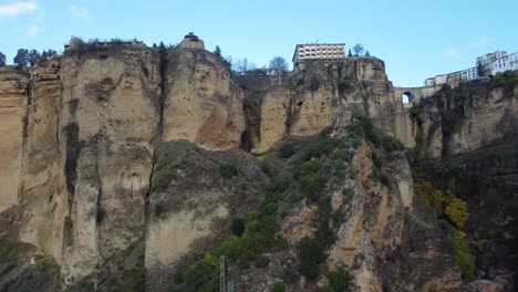 Rocky-cliff-with-deep-valley-and-city-buildings-of-Ronda-on-top,-aerial-view