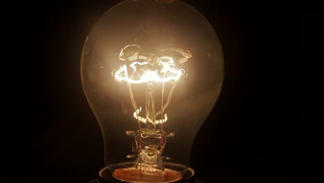 Close-up-of-light-bulb-lighting-up-in-the-dark,-thin-metal-filament-sits-in-the-middle-of-the-bulb-and-shining-periodically