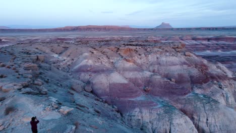 hiker-and-shorts-and-a-red-T-shirt-walking-over-a-mountain-spine-the-landscape-of-red-and-blue-rocks-at-blue-hour-in-bentonite-hills-utah-hanksville