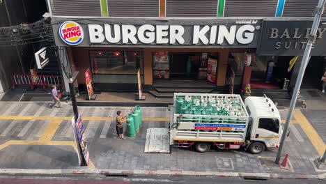 Trabajador-Cargando-Cilindros-De-Gas-Al-Camión-Fuera-De-La-Cadena-Burger-King-En-Silom-Soi-2,-Bangkok,-Tailandia