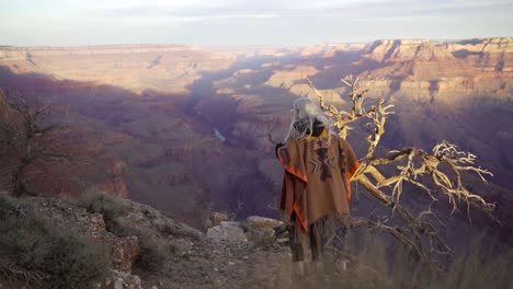 Back-view-of-tourist-hiker-girl-in-brown-orange-blanket-with-traditional-pattern-with-blond-hair-walks-on-edge-cliff-and-overlooking-grand-canyon,-panoramic-view