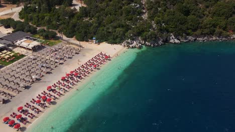 Drone-flying-across-Myrtos-beach-in-Greece,-full-of-beach-chairs
