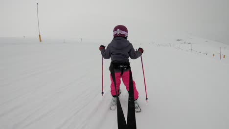 Young-girl-hold-in-straps-by-parent-while-learning-to-ski-downhill