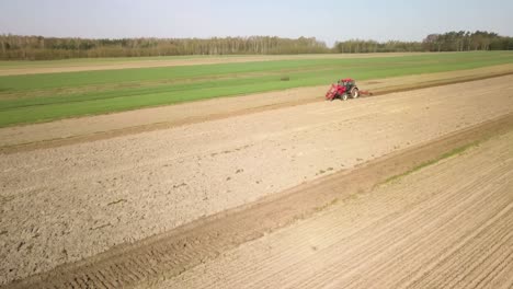 Luftaufnahme-Eines-Roten-Traktors,-Der-Auf-Dem-Landwirtschaftlichen-Feld-Arbeitet-Und-Das-Land-Für-Die-Aussaatsaison-Im-Frühling-Vorbereitet