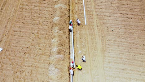 aerial-top-angle-view-of-Indian-labor-fitting-water-pipeline-into-the-pit-at-agricultural-land,-putting-pipeline-into-digging-for-fittings