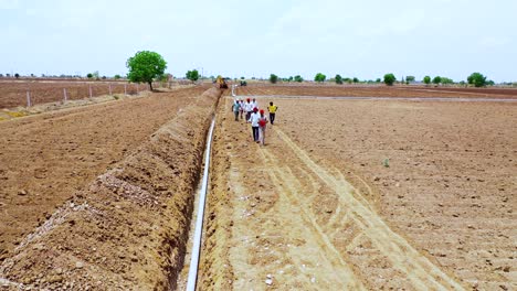 Aerial-camera-moving-forward,-head-shot-of-the-Indian-farmer-working-water-drainage-pipeline-at-hot-summer-seasons