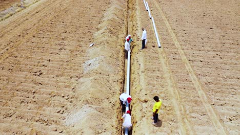 Aerial-camera-moving-top-into-Indian-farmer-and-labor-working-of-water-drainage-pipeline-at-hot-summer-seasons