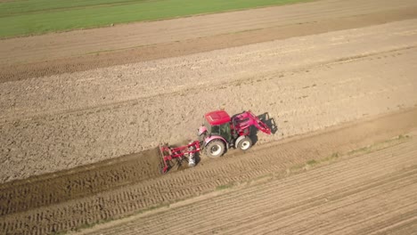 Antena-Sobre-Tractor-Rojo-Arando-Preparando-La-Tierra-En-El-Campo,-Concepto-Agrícola