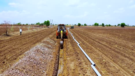 Aerial-camera-moving-backward-to-excavation-machine-working-of-digging-an-agricultural-land-for-water-system-solution-at-summer-time