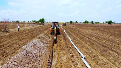 Luftbildkamera-Bewegt-Sich-Rückwärts-Zur-Aushubmaschine,-Die-Im-Sommer-Ein-Landwirtschaftliches-Land-Für-Eine-Wassersystemlösung-Gräbt