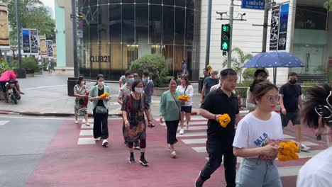 Guía-Turístico-Local-Liderando-A-Un-Grupo-De-Turistas-Con-Guirnaldas-De-Flores-Cruzando-La-Calle-Hacia-El-Famoso-Santuario-De-Erawan-En-El-Distrito-De-Ratchaprasong-En-El-Centro-De-Bangkok,-Tailandia