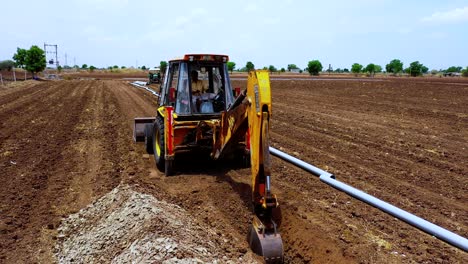 Close-up-shot-of-excavation-digging-deep-soil-at-farm,-aerial-follow-shot-of-excavation