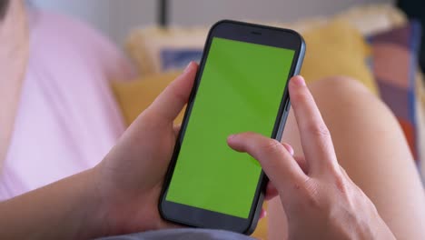 Close-up-Caucasian-hand-scroll-on-green-screen-on-mobile-phone,-lying-on-couch