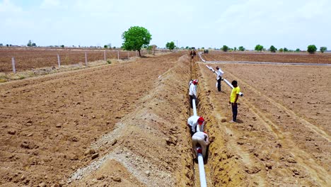 Aerial-camera-moving-above-the-water-drainage-pipeline-fittings-on-the-agricultural-land,-farmer-working-at-hot-seasons-in-the-farm-land