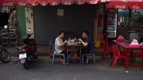 Couple-happily-dined-food-on-the-roadside-and-chit-chatted-in-the-street-restaurants-at-Yaowarat-Chinatown,-Bangkok,-Thailand