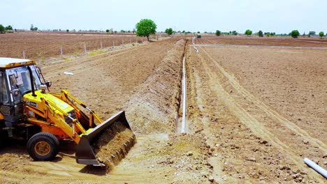 Vista-Aérea,-Vista-Frontal-De-La-Máquina-De-Movimiento-De-Tierras-Que-Cubre-La-Tubería-De-Agua-Subterránea-Con-Tierra-En-La-India