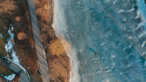 Aerial-shot-of-walking-path-by-frozen-icy-blue-lake