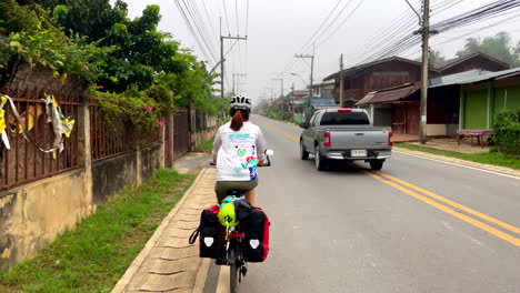 Eine-Einsame-Radfahrerin,-Die-Mit-Anderen-Vorbeifahrenden-Fahrzeugen-Auf-Einer-Städtischen-Straße-In-Der-Provinz-Nan,-Thailand,-Fährt