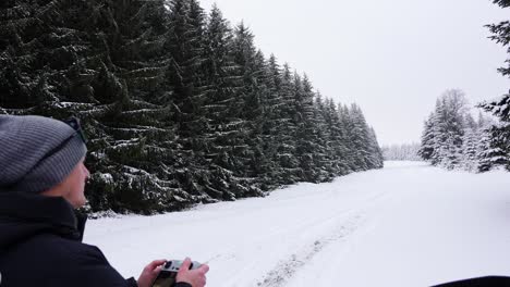 Man-flying-a-drone-in-the-forest-covered-snow---handheld-shot