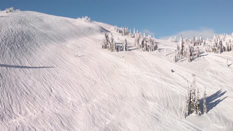 Aerial-panoramic-view-of-a-snowmobile-riding-on-a-snowed-hill-on-a-sunny-day-in-Revelstoke,-Canada